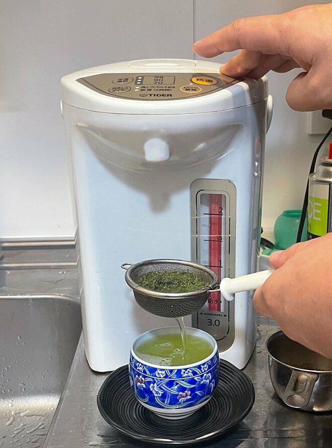 お茶っぱを入れた茶こしを右手で持ち、電気ポットからお湯を茶こしから湯呑みに注ぐ様子 (画像／編集部)