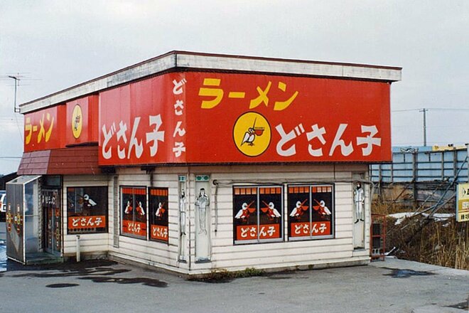 1977年当時のどさん子ラーメンの建物外観写真 赤い看板にペリカンのマークが書かれている (写真提供：アスラポート株式会社)